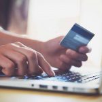 Woman typing on a computer while holding her credit card